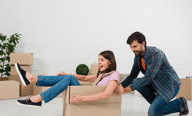 husband-pushing-his-wife-sitting-cardboard-box 1